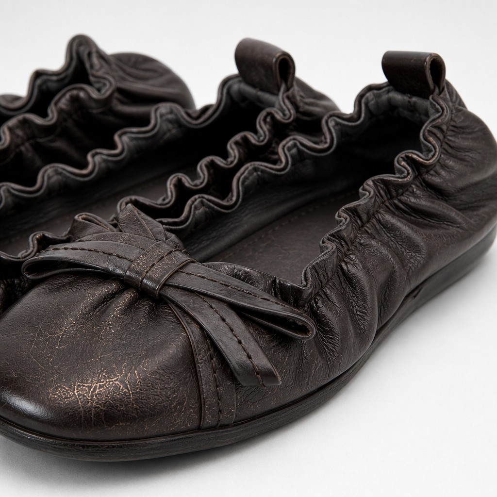 Close-up of black flat shoe upper with bow and elasticized edge