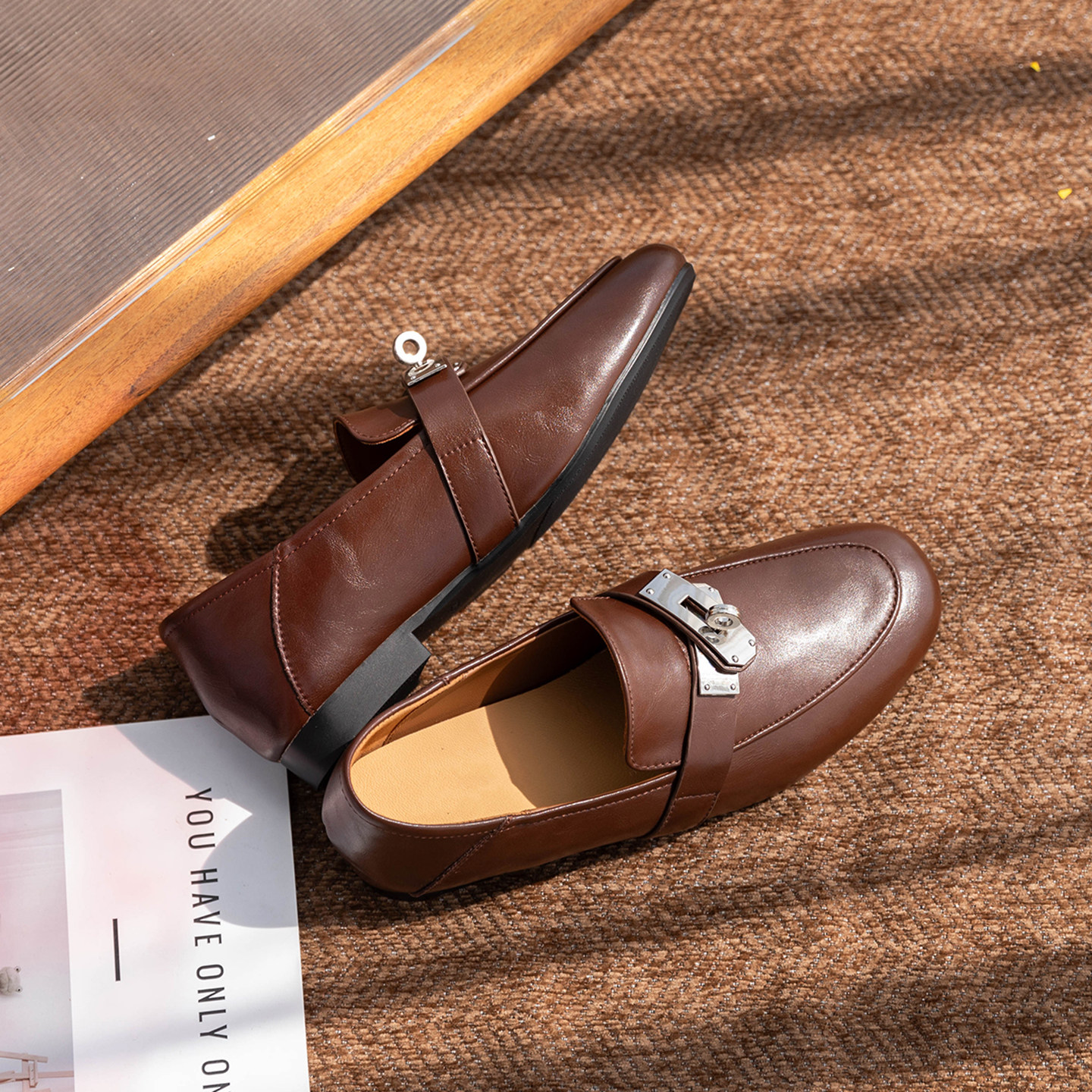 Des mocassins marrons mis en scène dans un décor de style de vie avec des tissus et des accessoires.