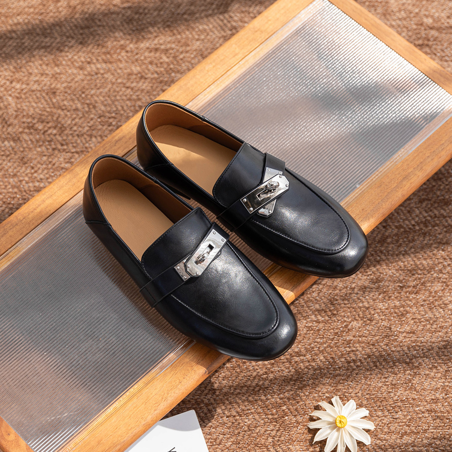 Une paire de mocassins noirs est présentée dans une scène en tissu mise en scène.