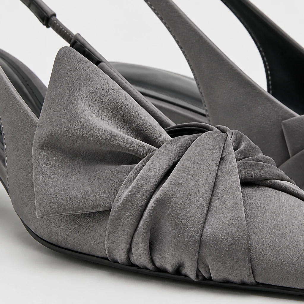Close do material cinza da bomba tipo slingback, detalhe de laço, bico pontiagudo e construção de calcanhar