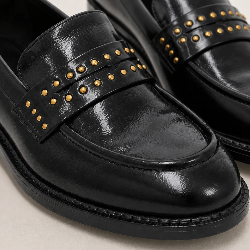 Close-up detail of glossy black loafer material and studded strap